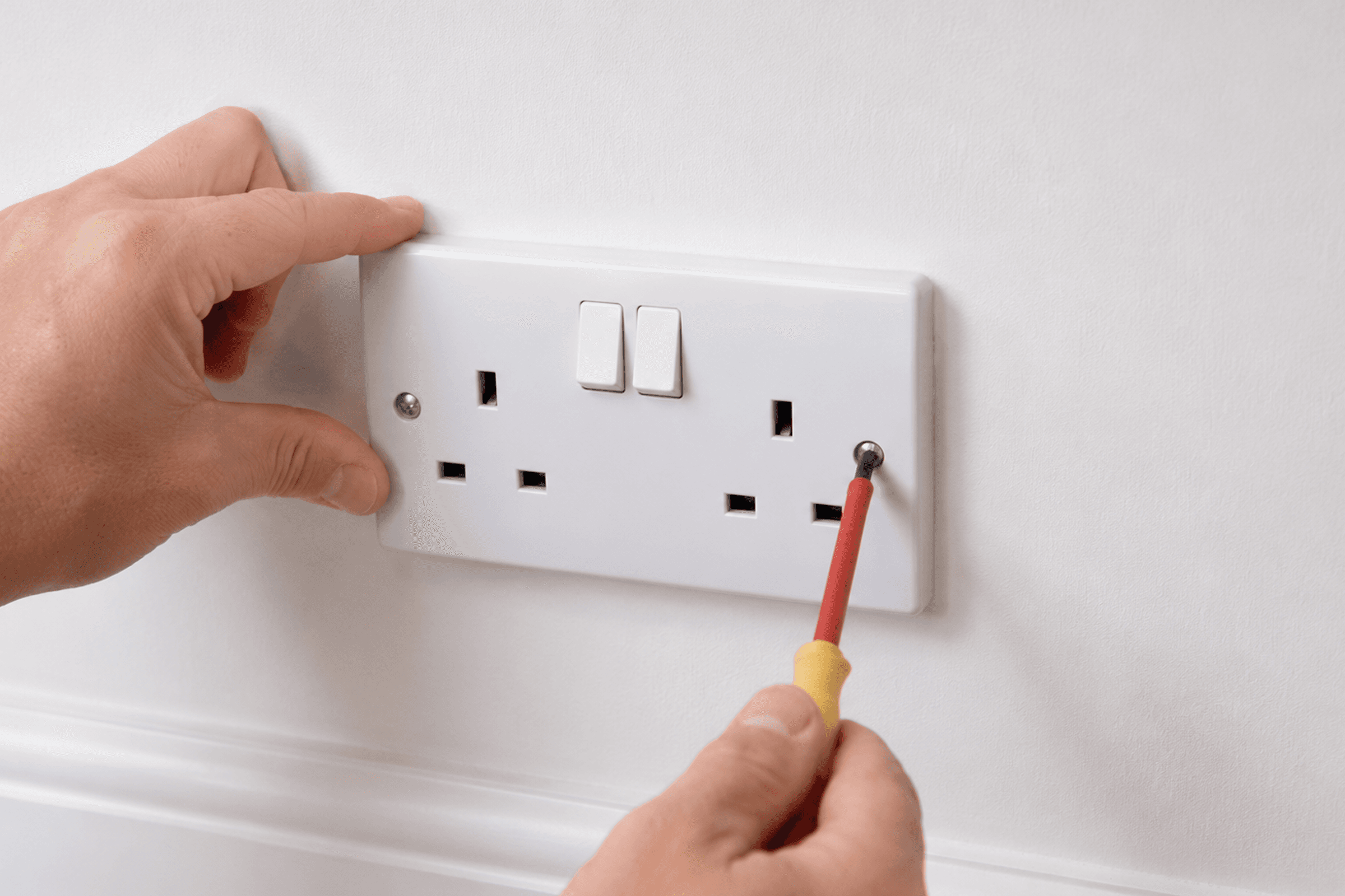 A person installing a switch next to an electrical socket with a drill.