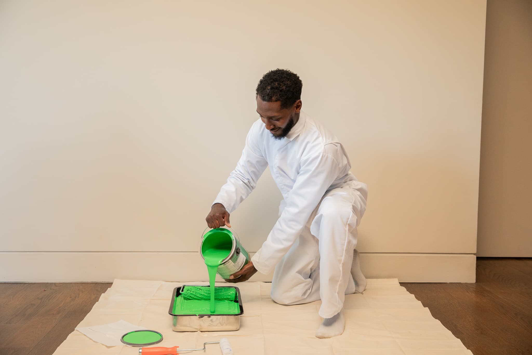 Man in white protective suit pouring green paint into a paint tray