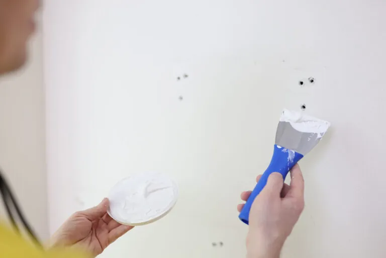 Person filling small holes in a wall with spackle and a putty knife