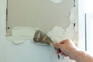 Thick layers of spackle being applied to a wall with a putty knife