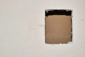 Large hole in wall with a board behind it for support