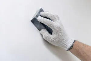 Hand in a glove smoothing spackle with a sanding block